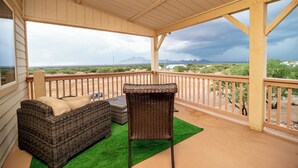 Un balcon abrité, doté de meubles en osier, d’un tapis vert et offrant une vue sur un paysage désertique avec des montagnes à l’horizon.