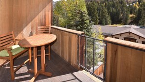 A wooden balcony with a table and chairs, overlooking a forested valley.