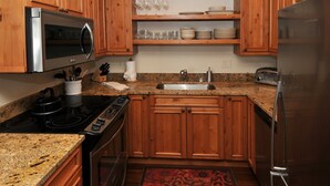 Una cocina con armarios de madera, un refrigerador de acero inoxidable, un microondas, una estufa y un lavamanos.