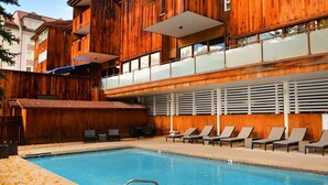 A wooden building with a pool and lounge chairs.