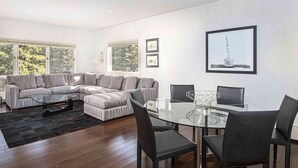 A modern living room with a sectional sofa, a glass coffee table, and a dining area with a glass table and chairs.