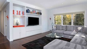A modern living room with a grey sofa, a glass coffee table, and a white entertainment unit with a flat-screen TV.