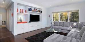 Relax in comfort with a large flat-screen TV, plush sofa, and a view of the surrounding trees.