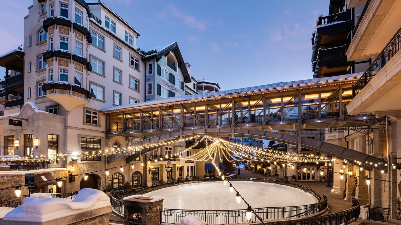 A multi-story building with a central courtyard featuring a snow-covered circular area, surrounded by balconies and string lights.