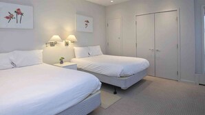 A hotel room with two beds, a nightstand with lamps, a door, and artwork on the walls.