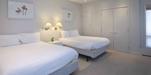 Two single beds with bedside tables and lamps, a nightstand, and a neutral color palette.