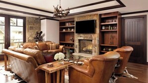 A cozy living room with a stone fireplace, leather furniture, and a mounted TV. - Luxury 3 Bedroom Residence at The Four Seasons in Vail Village (Vail)