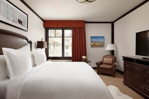 Une chambre d’hôtel avec un grand lit, une télévision, un bureau avec une lampe, une chaise et une fenêtre avec des rideaux.