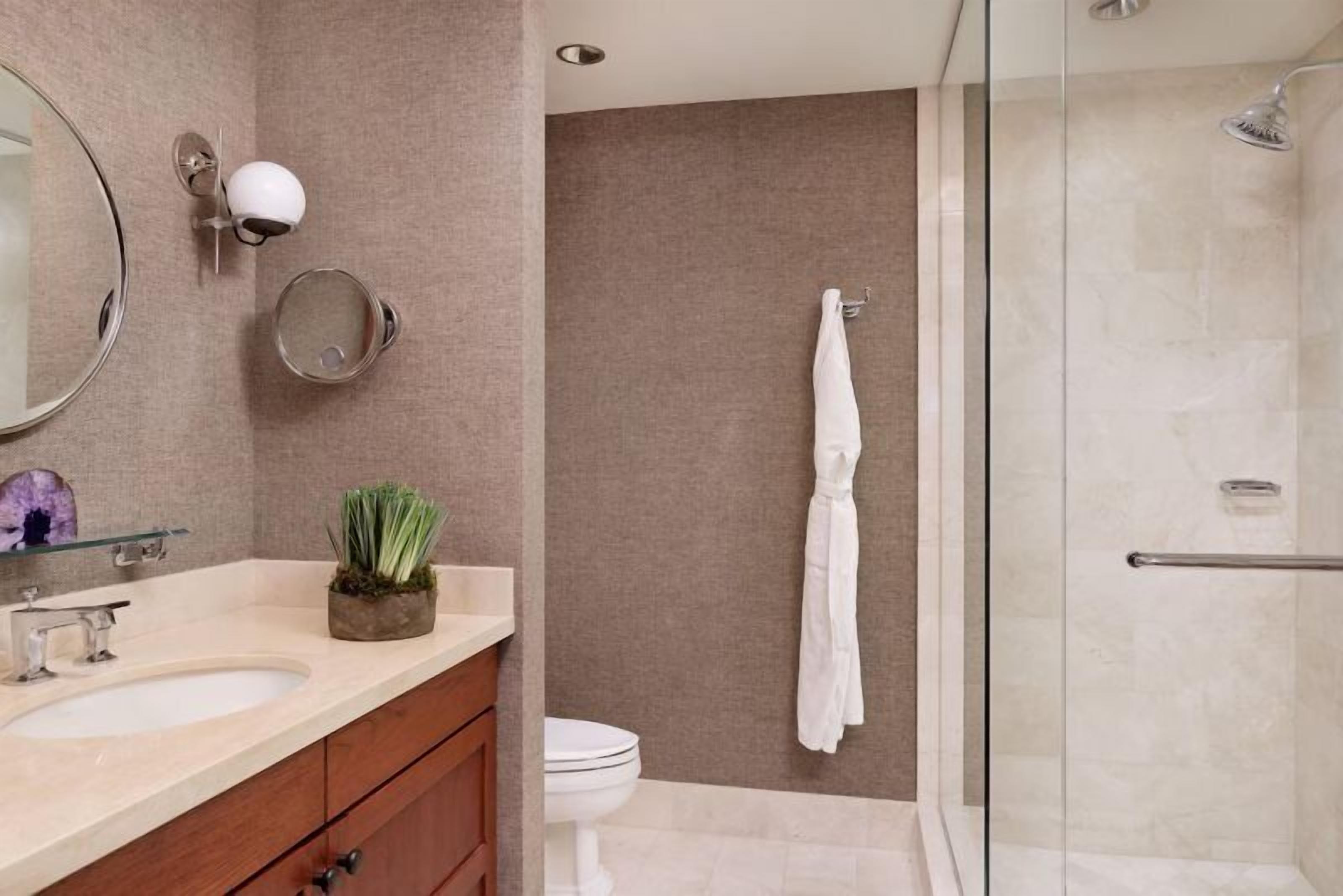 A modern bathroom with a glass shower enclosure, a white toilet, and a vanity with a sink and mirror.