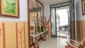 Un couloir avec une chaise en bois, un miroir et un vase contenant des plantes séchées.