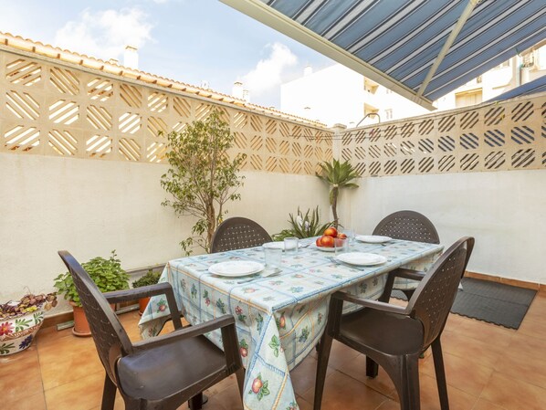 Een terras met een tafel voor twee personen, omringd door stoelen, onder een blauw zonnescherm.