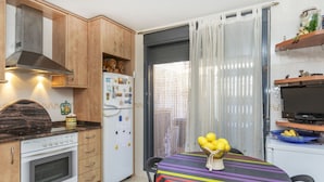 Une cuisine compacte avec des meubles en bois, un four encastré, un réfrigérateur et un coin repas agrémenté d’une nappe à rayures.