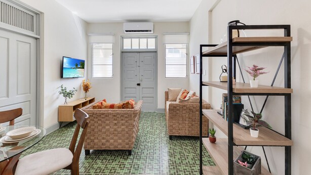 Una sala de estar con dos sofás de mimbre, una mesa de comedor de vidrio y una estantería de madera.