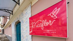 Un letrero rojo con texto blanco que dice 'Picaflor' y 'Estancias Culturales en Santurce, PR' en la fachada de un edificio.
