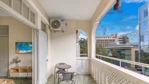 Un balcón con vistas a edificios, una mesa con sillas, una planta pequeña y un cuadro en la pared.