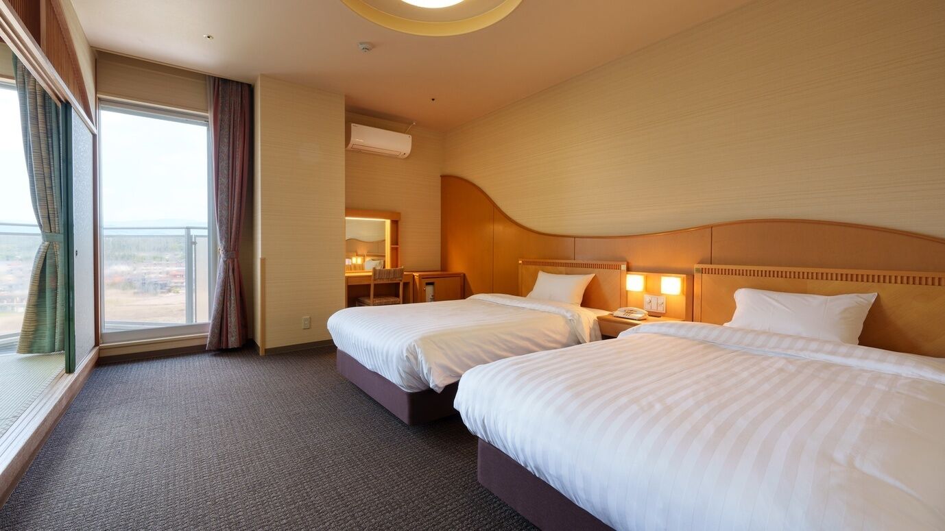Ein Hotelzimmer mit zwei Betten, einem Schreibtisch, einem Stuhl, einem Spiegel und einem Fenster mit Vorhängen.