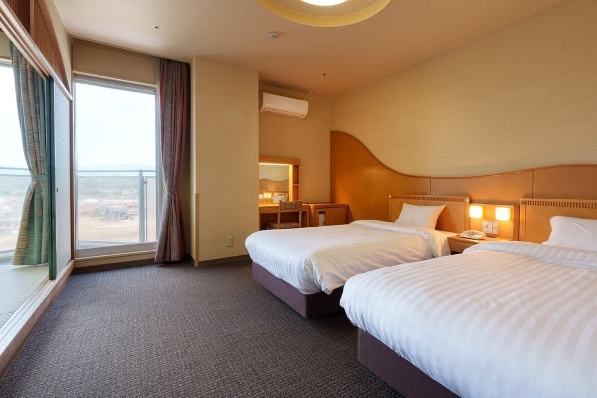 Ein Hotelzimmer mit zwei Betten, einem Schreibtisch, einem Stuhl, einem Spiegel und einem Fenster mit Vorhängen.