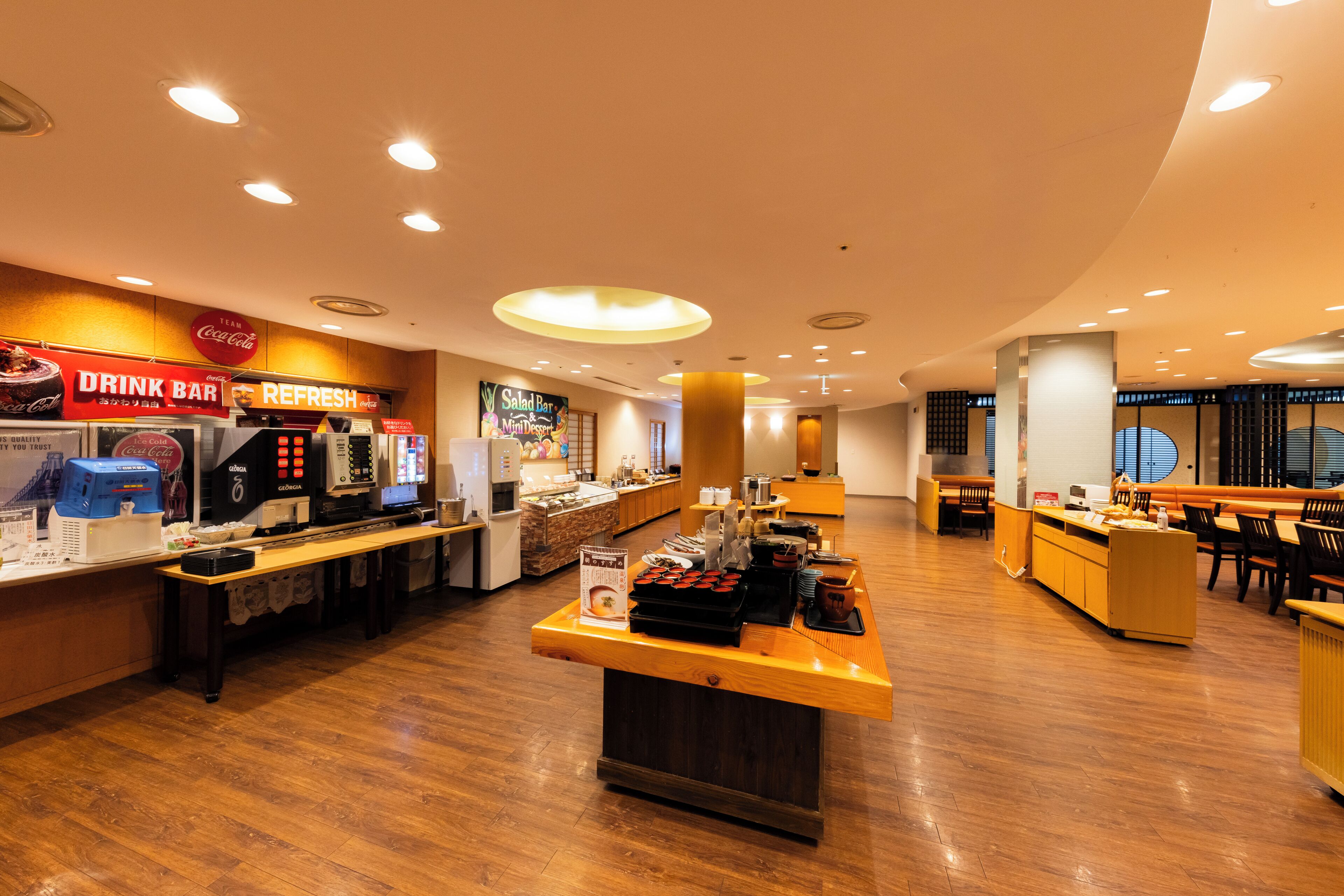 A restaurant with a drink bar, a salad bar, and a counter with food items.