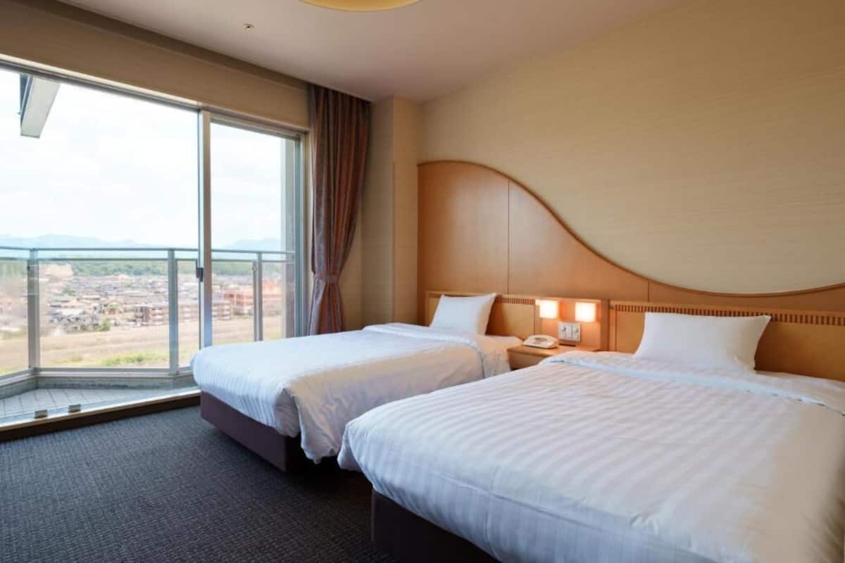 Ein Hotelzimmer mit zwei Betten, einem großen Fenster mit Blick und einem gewölbten Kopfteil.