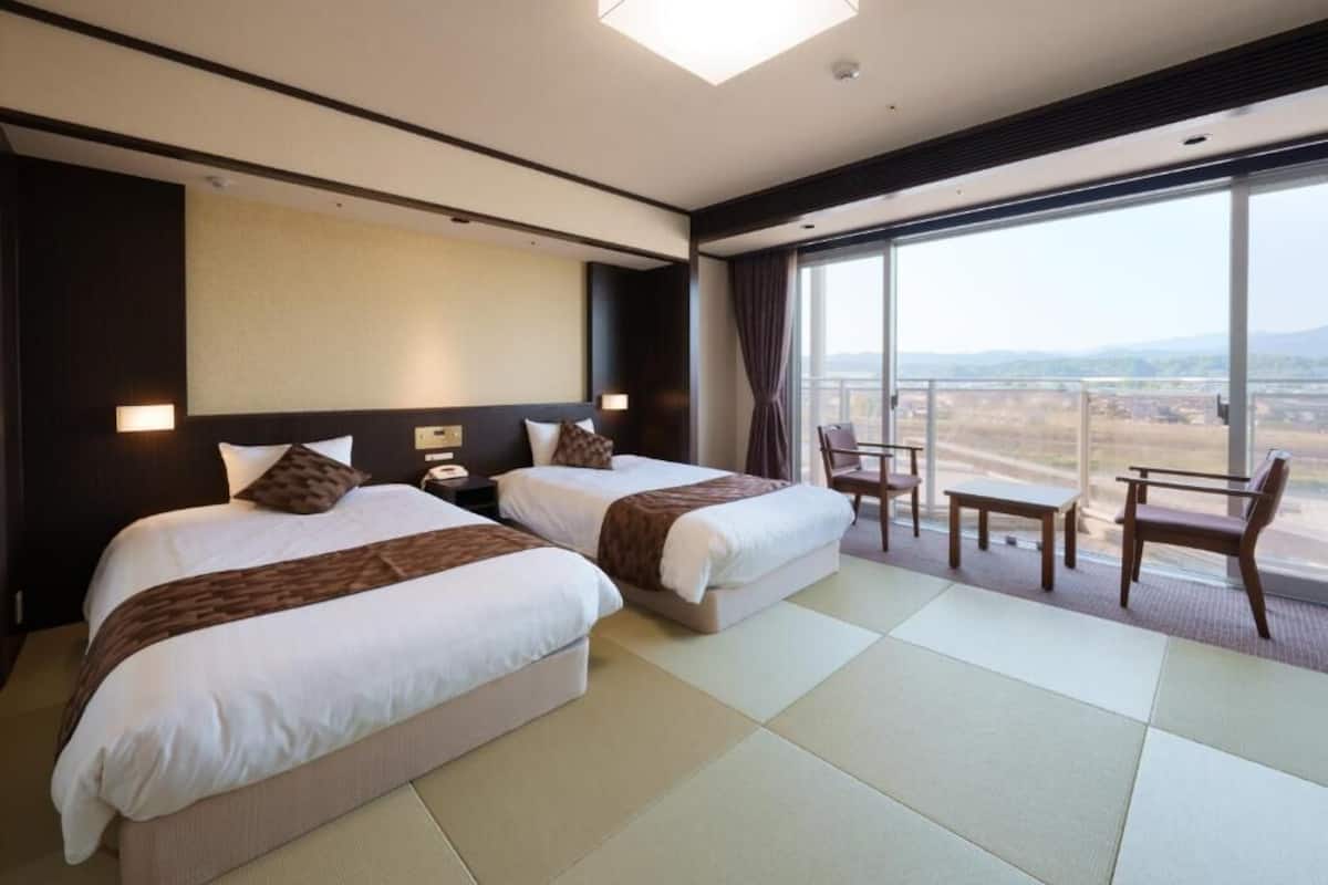 Ein Hotelzimmer mit zwei Betten, einem großen Fenster mit Blick und einer Sitzecke mit Tisch und Stühlen.