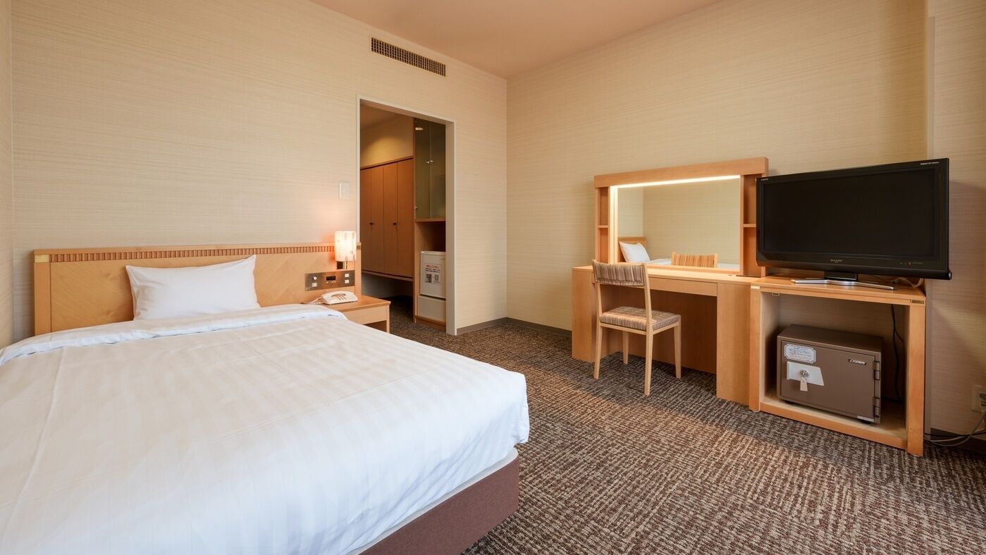 Ein Hotelzimmer mit Bett, Schreibtisch, Stuhl, Fernseher und einer Minibar.