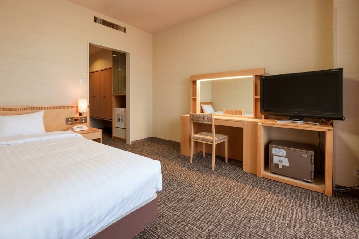 Ein Hotelzimmer mit Bett, Schreibtisch, Stuhl, Fernseher und einer Minibar.