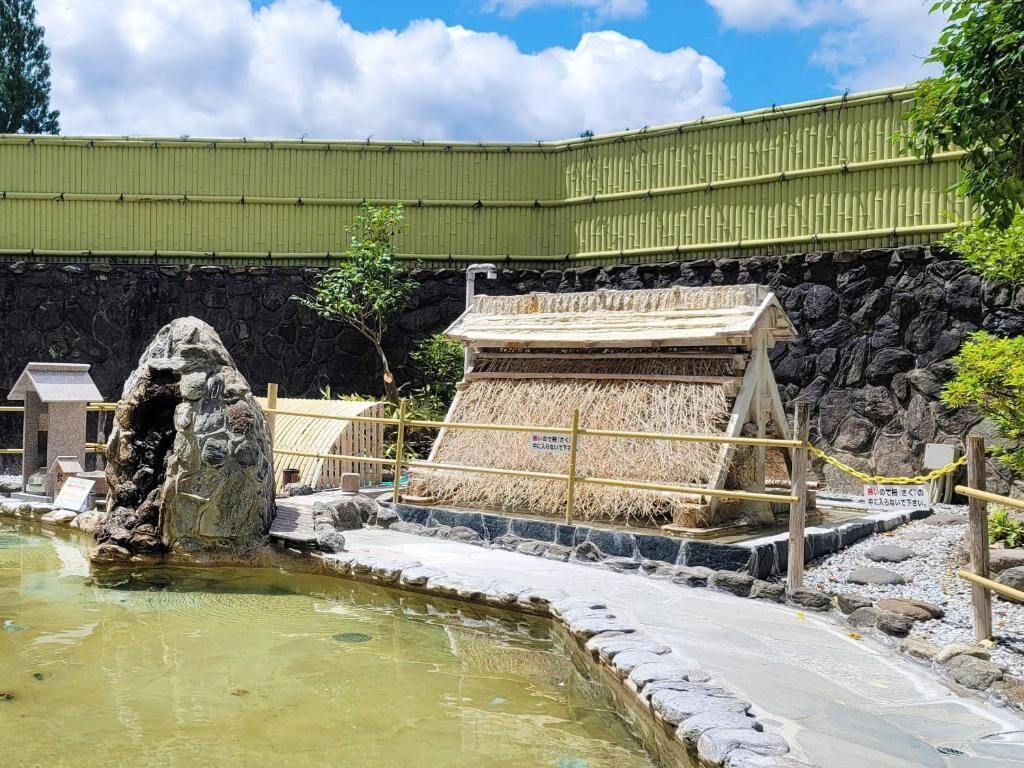 A traditional Japanese garden with a rock formation, a small pond, and a thatched structure.