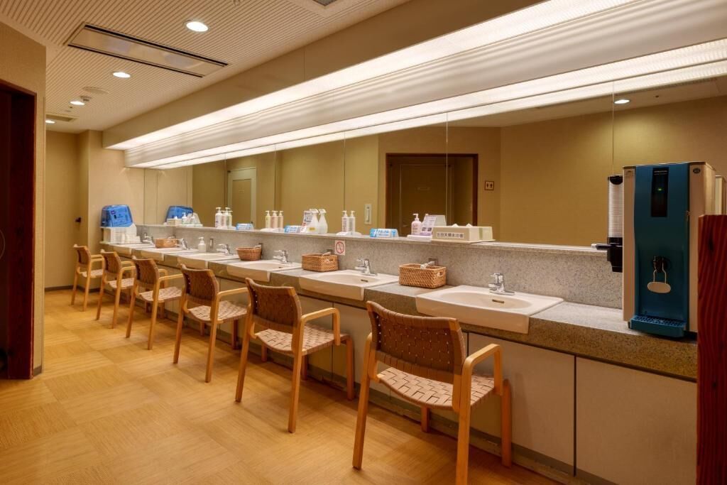 Un baño de hotel con varios lavamanos, sillas de mimbre y un espejo grande.