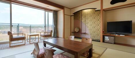 Habitación de hotel con una amplia mesa de comedor, sillas, un televisor y vistas al paisaje.