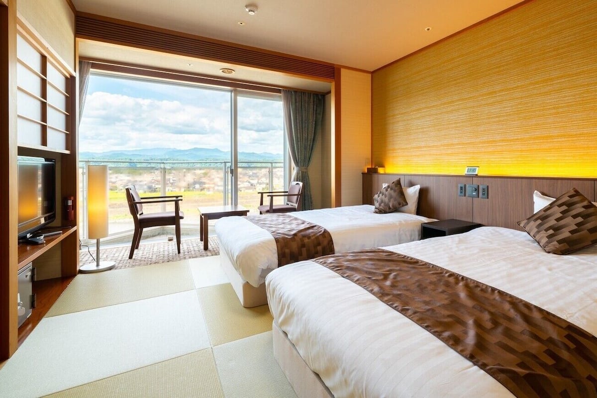 Ein Hotelzimmer mit zwei Betten, einem Fernseher, einem Schreibtisch und Blick ins Freie.
