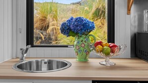 A kitchen with a stainless steel sink, a vase with blue flowers, and a fruit bowl on the counter. - Bacardi Heights Waikaia by Tiny Away (Waikaia)