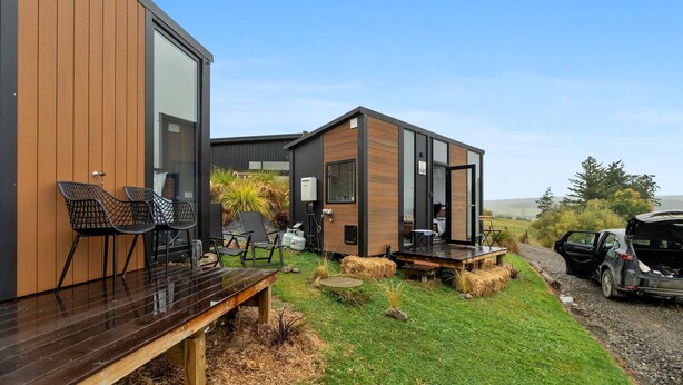 A modern building with large windows, outdoor seating, and a gravel path. - Bacardi Heights Waikaia by Tiny Away (Waikaia)