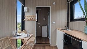 A modern kitchen with a wooden countertop, a sink, and a dishwasher. There is a dining area with a table and chairs, and a view of the outdoors through large windows. - Bacardi Heights Waikaia by Tiny Away (Waikaia)