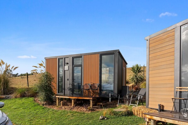 Un edificio moderno y compacto con amplios ventanales, una terraza de madera y asientos exteriores.