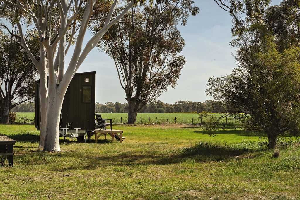 Una cabana de fusta rústica amb un petit balcó, envoltada d'arbres i camps oberts.