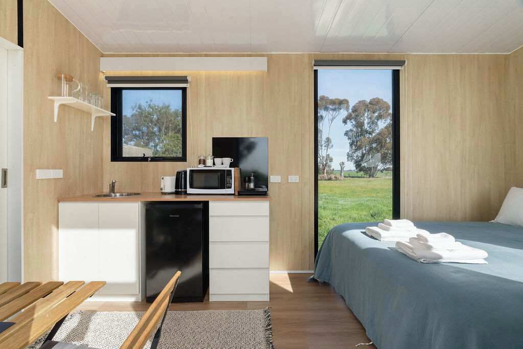 A modern bedroom with a bed, a small kitchenette, and a view of the outdoors.