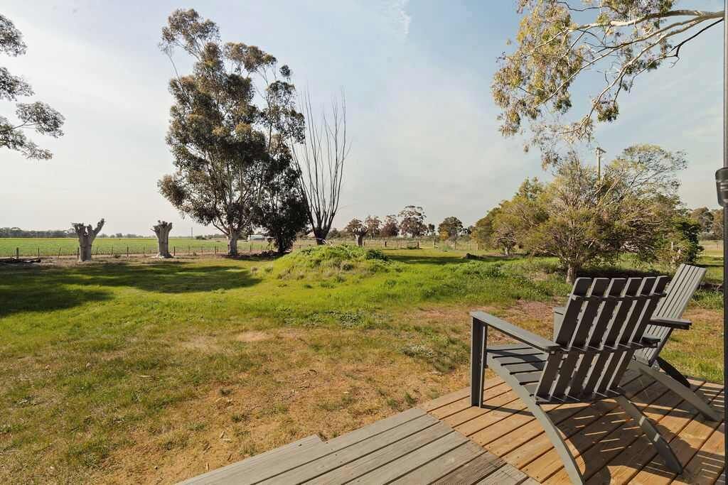 A deck with a chair, surrounded by a grassy area with trees and a fence in the background.