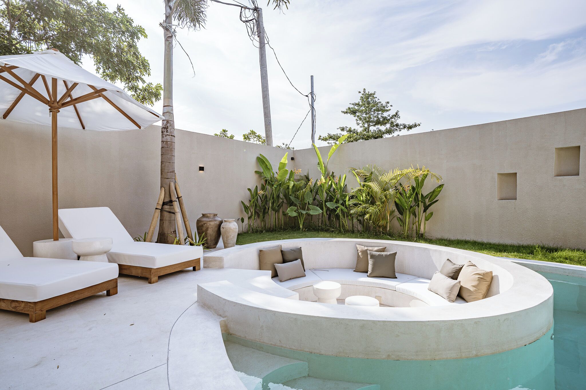 A poolside area with lounge chairs, a seating area with cushions, and a palm tree.
