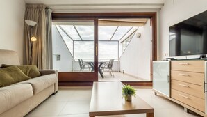 Een moderne woonkamer met een bank, een salontafel, een televisie en een balkon met een tafel en stoelen.