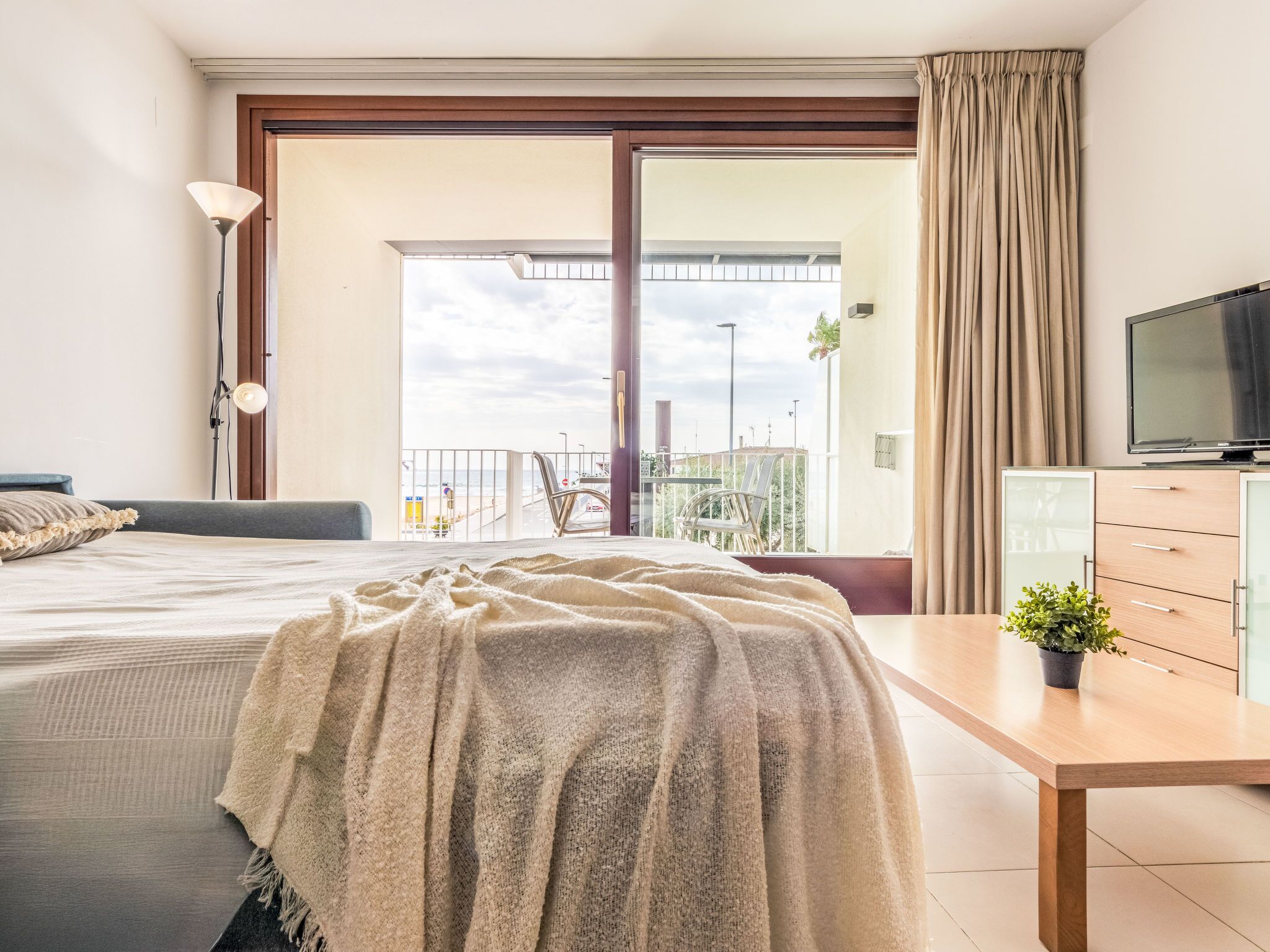 Habitación de hotel con cama, escritorio, televisión y balcón con vista a la playa.