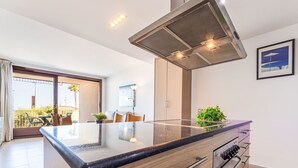 Une cuisine moderne dotée d’un îlot central, d’appareils électroménagers en acier inoxydable et d’une porte-fenêtre coulissante donnant sur un espace extérieur.