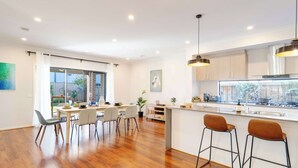 A modern kitchen with a large island, bar stools, and a dining area with chairs and a table. - Lux Clyde North Super Spacious Retreat (Clyde North)