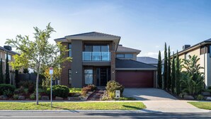 A two-story house with a garage, a front yard with landscaping, and a clear sky. - Lux Clyde North Super Spacious Retreat (Clyde North)