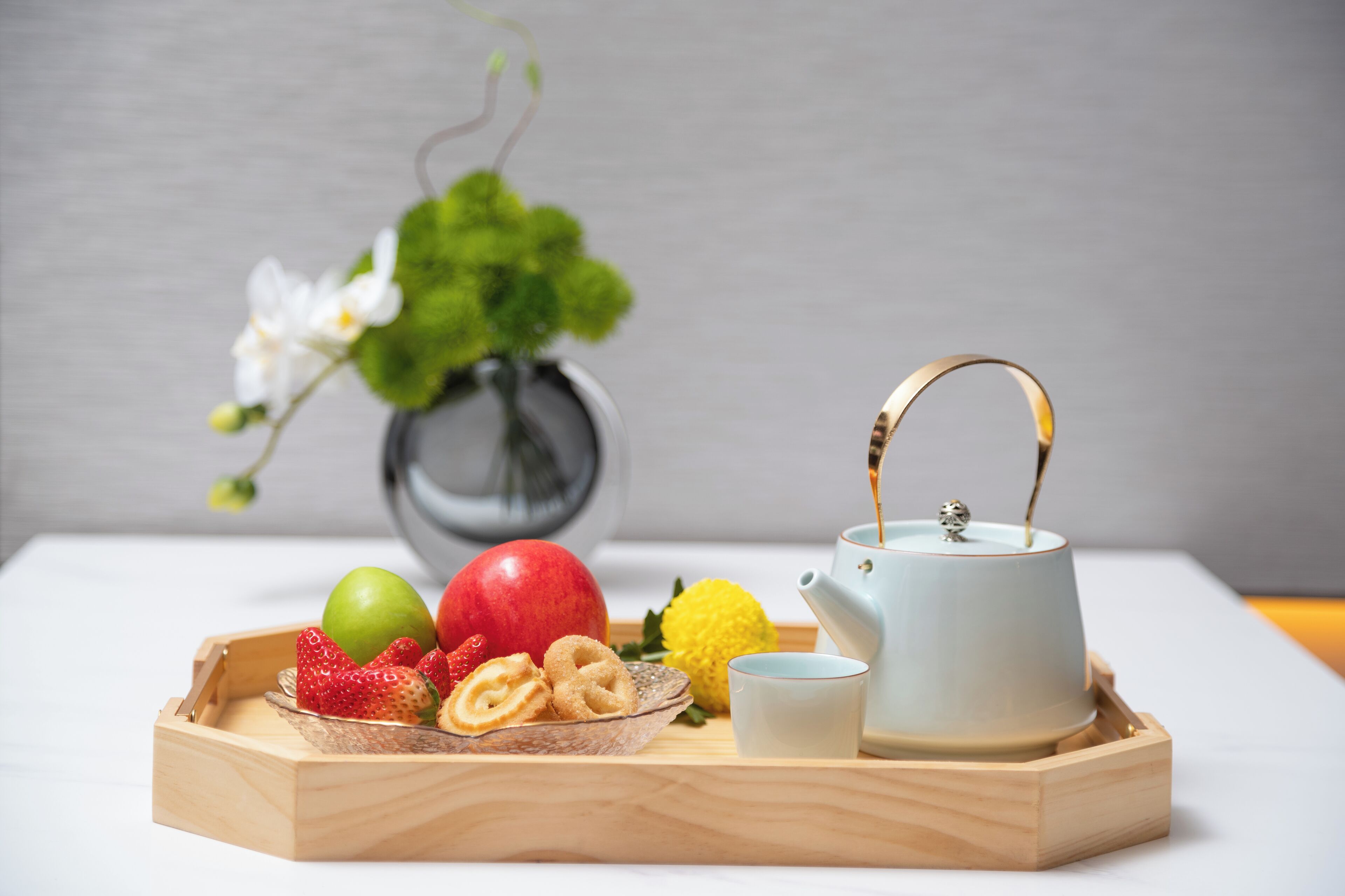 A wooden tray with fruits, a teapot, and a cup on a table.