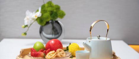 A wooden tray with fruits, a teapot, and a cup on a table.