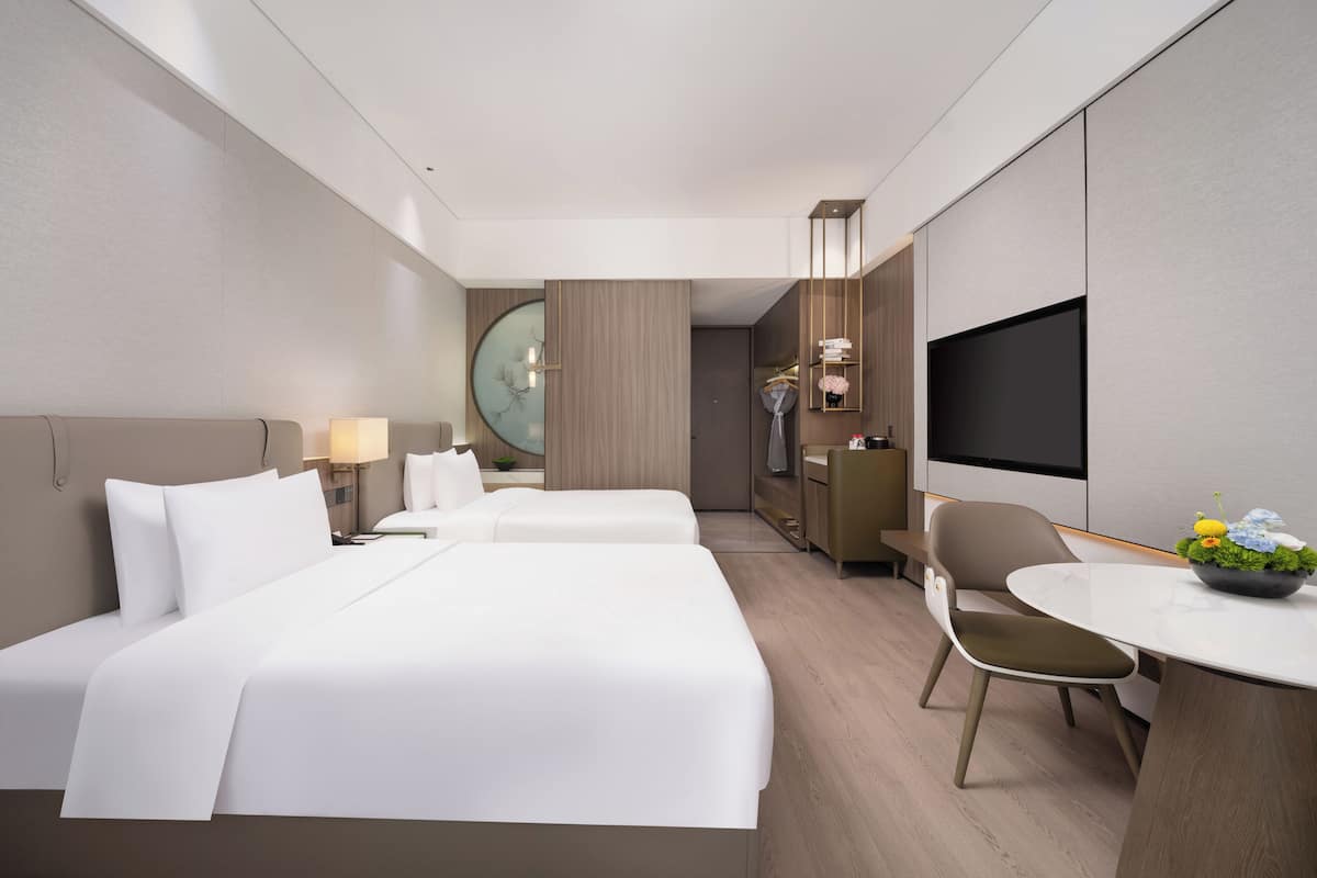 A hotel room with two beds, a desk, a chair, a TV, and a large mirror.