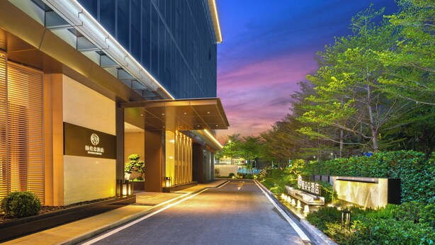 A modern hotel entrance with a well-lit pathway, a signboard, and lush greenery. - EDDRER HOTEL (Shenzhen)