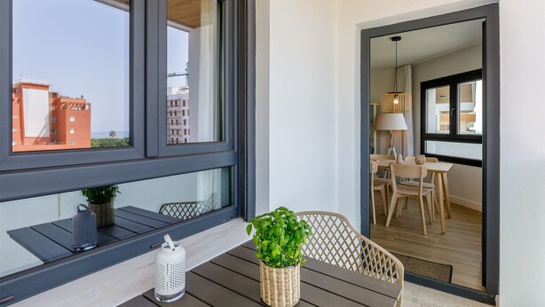 Ein Balkon mit Blick auf Gebäude, ein Korbwicker-Korb mit Grünpflanzen, ein weißer Kerzenständer und ein Holzstuhl.