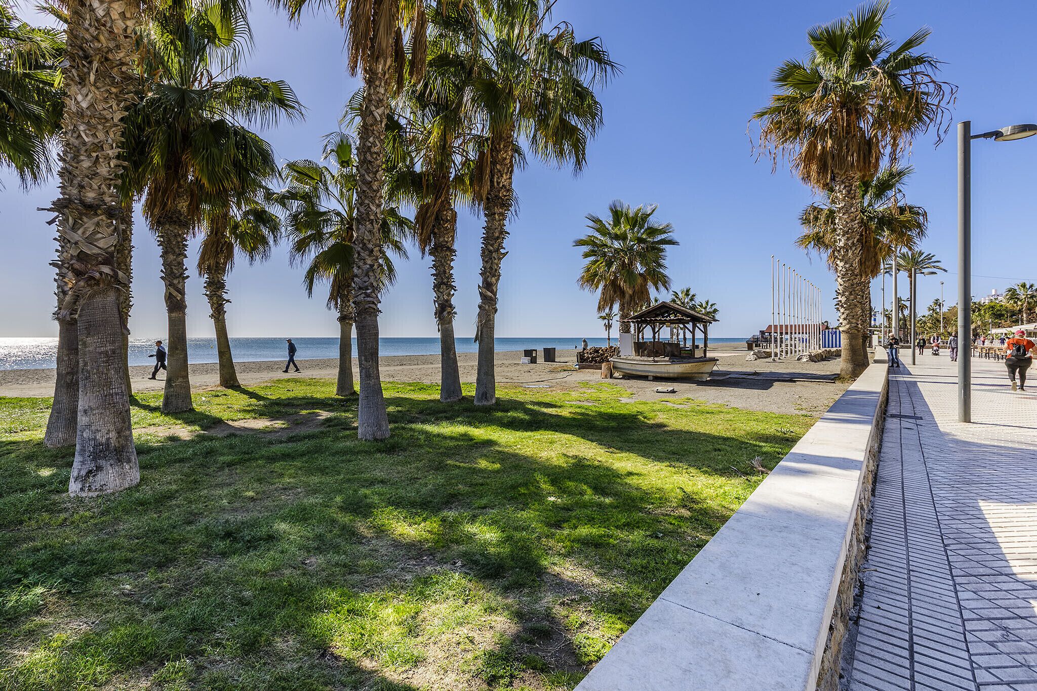 A beachside promenade with palm trees, a gazebo, and a clear view of the sea.