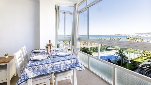 A balcony with a dining table set for two, overlooking a coastal view with palm trees and a clear sky. - A&N Algarrobo Beach 5 (Algarrobo Costa)